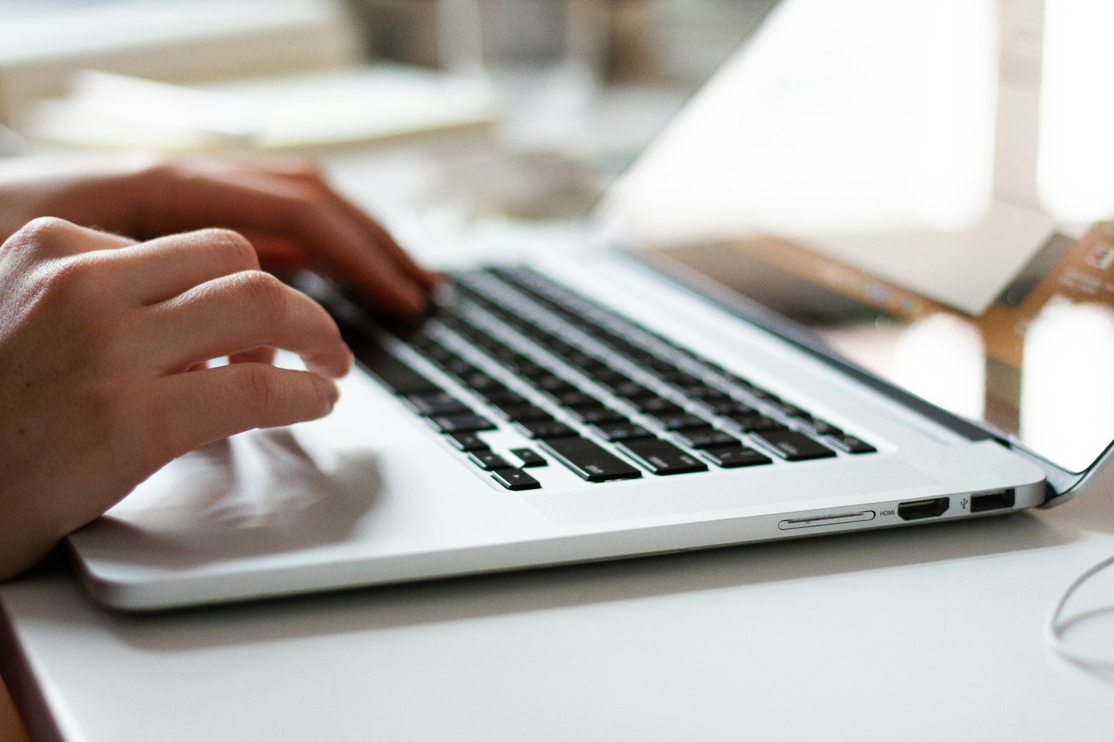 Hands typing on a laptop keyboard in a bright workspace